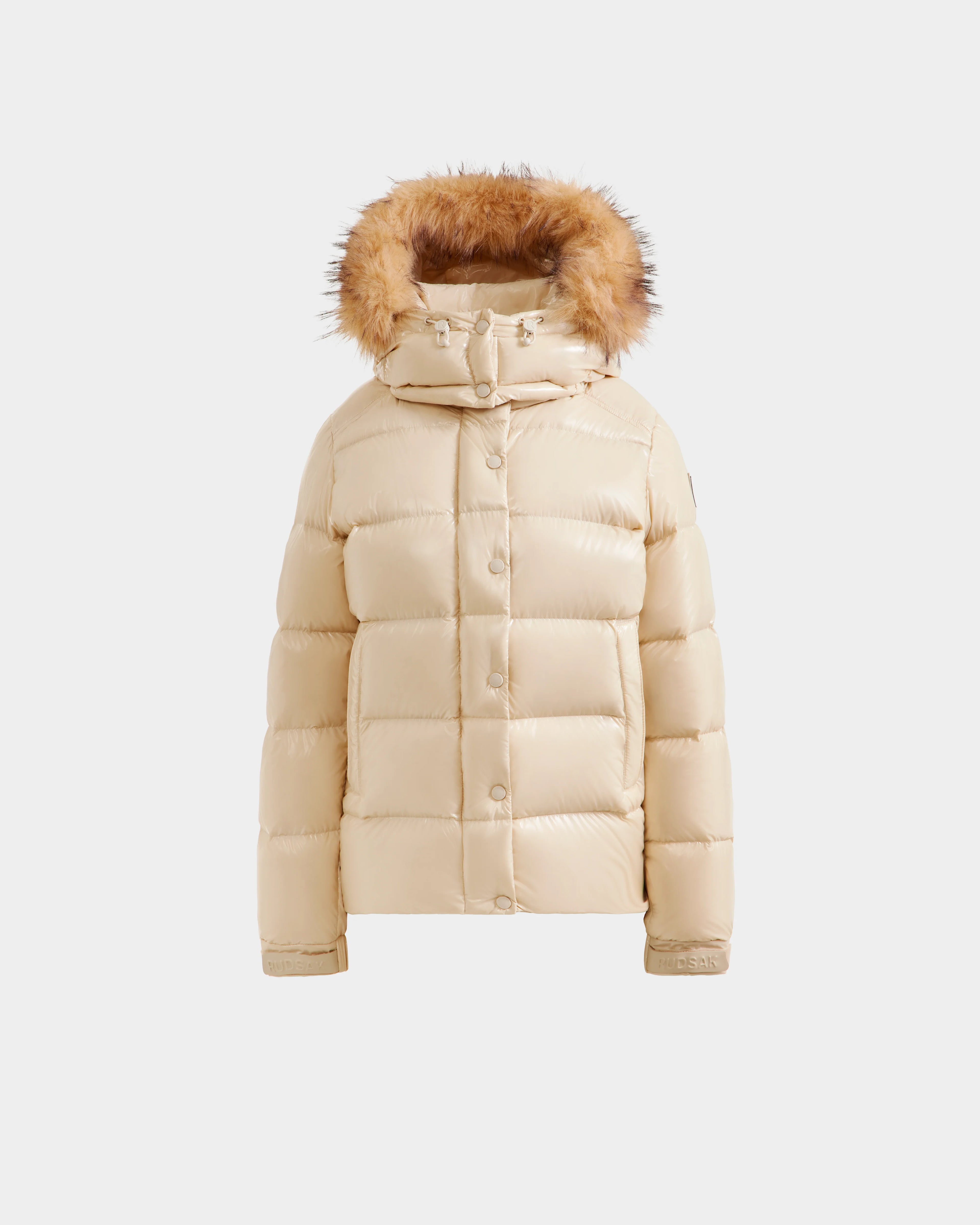 The Rudsak BREE S - L125583 Vanilla is a beige women’s down puffer jacket with a fur-lined removable hood, front snap buttons, and horizontal quilting, shown against a plain white background.