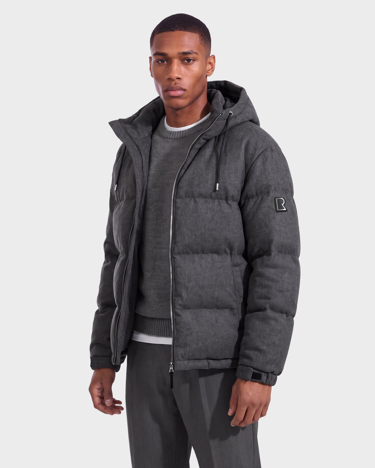 A man wearing the Rudsak STERLING W - 6126760 Heather Charcoal puffer jacket stands against a plain light background, looking at the camera.