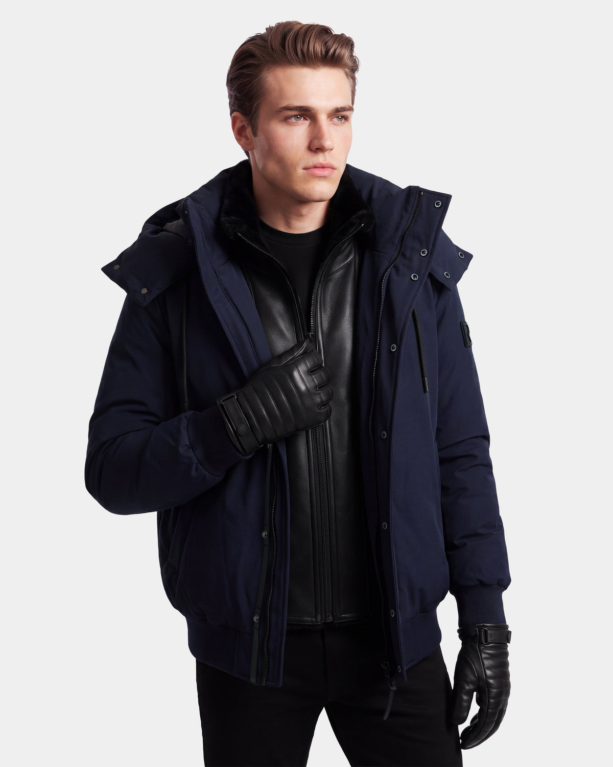 A man in the Rudsak WILL - 6126561 Navy bomber jacket and black leather gloves stands against a plain background, looking to the side. He wears a black shirt and a black zippered inner jacket.