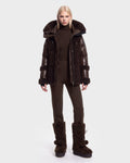 A person stands facing forward, wearing the Rudsak MARISSA - 8126728 Espresso dark brown down insulated puffer coat with fur trim, paired with matching brown pants and large brown fur boots—perfect winter outerwear. The background is plain white.