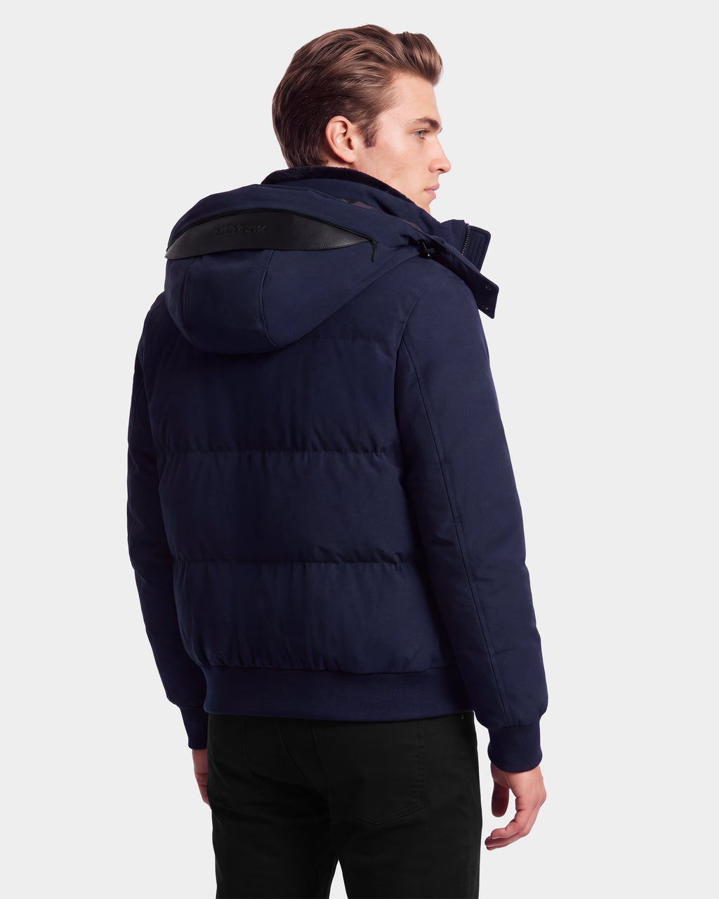 A person wearing the Rudsak WILL - 6126561 Navy puffer jacket, featuring RDS-certified down and a hood, stands facing away and slightly turned to the side against a plain white background.