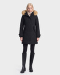 A person stands facing forward against a plain white background, wearing the Rudsak KEYSHIA - 8126517 Black women’s down parka with fur trim, paired with black leggings and tall black boots.