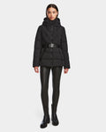 A woman faces forward against a white background, wearing the Rudsak ENZAH - 8124692 Black mid-length puffer jacket with a belt, paired with black faux leather leggings and black ankle boots.