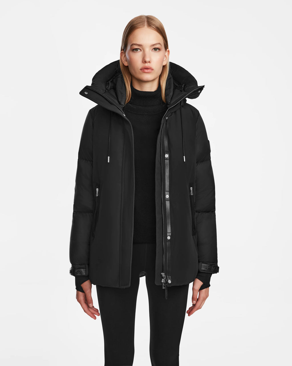 A woman with straight blonde hair wears the Rudsak LOLI - 8124507 Black parka and black pants, standing against a plain white background and looking directly at the camera with a neutral expression.