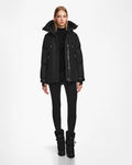 A woman faces forward against a plain white background, wearing the Rudsak LOLI - 8124507 Black womens down parka, paired with a black turtleneck, black leggings, and black winter boots.