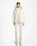 A woman faces forward in a Rudsak LOLI - 8124507 Iceland white winter parka, paired with earmuffs, a puffer jacket, turtleneck, leggings, and lace-up boots against a plain white background.