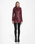A woman faces forward, wearing the Rudsak MARRY - L121003 Wine long puffer with hood, black leggings, and black ankle boots against a plain white background.
