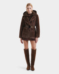 A woman faces forward in the Rudsak ASPEN F - 8125604 Mocha, a brown belted faux fur jacket with a removable down-insulated hood. She pairs it with a short brown dress and knee-high suede boots against a white background.