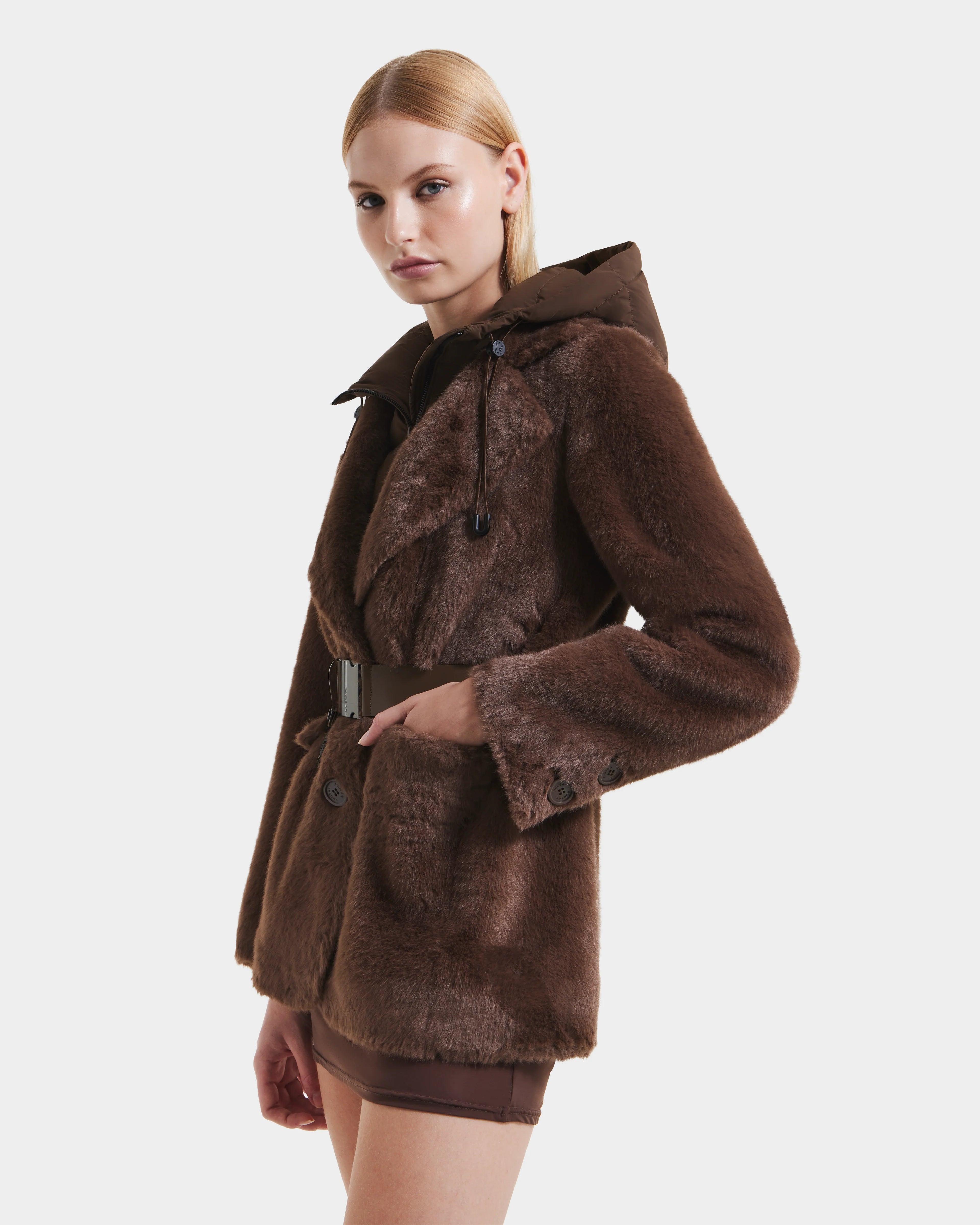 A woman models the Rudsak ASPEN F - 8125604 Mocha faux fur jacket with a belted waist and removable down-insulated hood, posing against a white background—a chic pick for any cold-weather wardrobe.