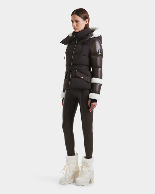 A woman models the Rudsak AUDREY - 8124582 Espresso brown down puffer jacket with white faux fur trim, paired with matching leggings and fur-lined boots against a plain white background.