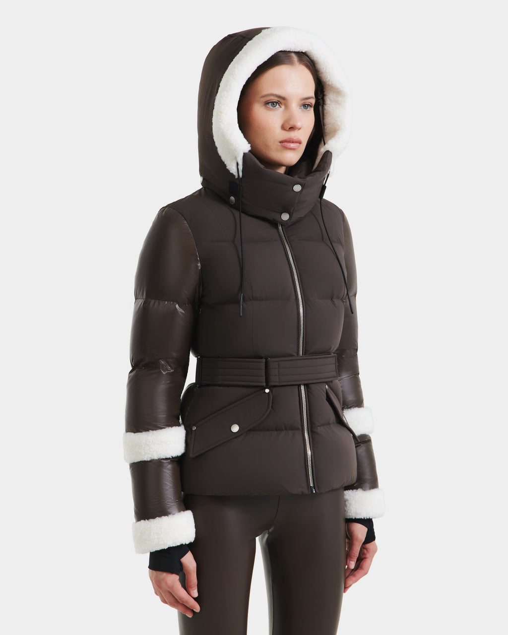 A woman wears the Rudsak AUDREY - 8124582 Espresso dark brown down puffer jacket with white faux fur trim and a wide waist belt. Filled with RDS certified down, it stands out against a plain white background.