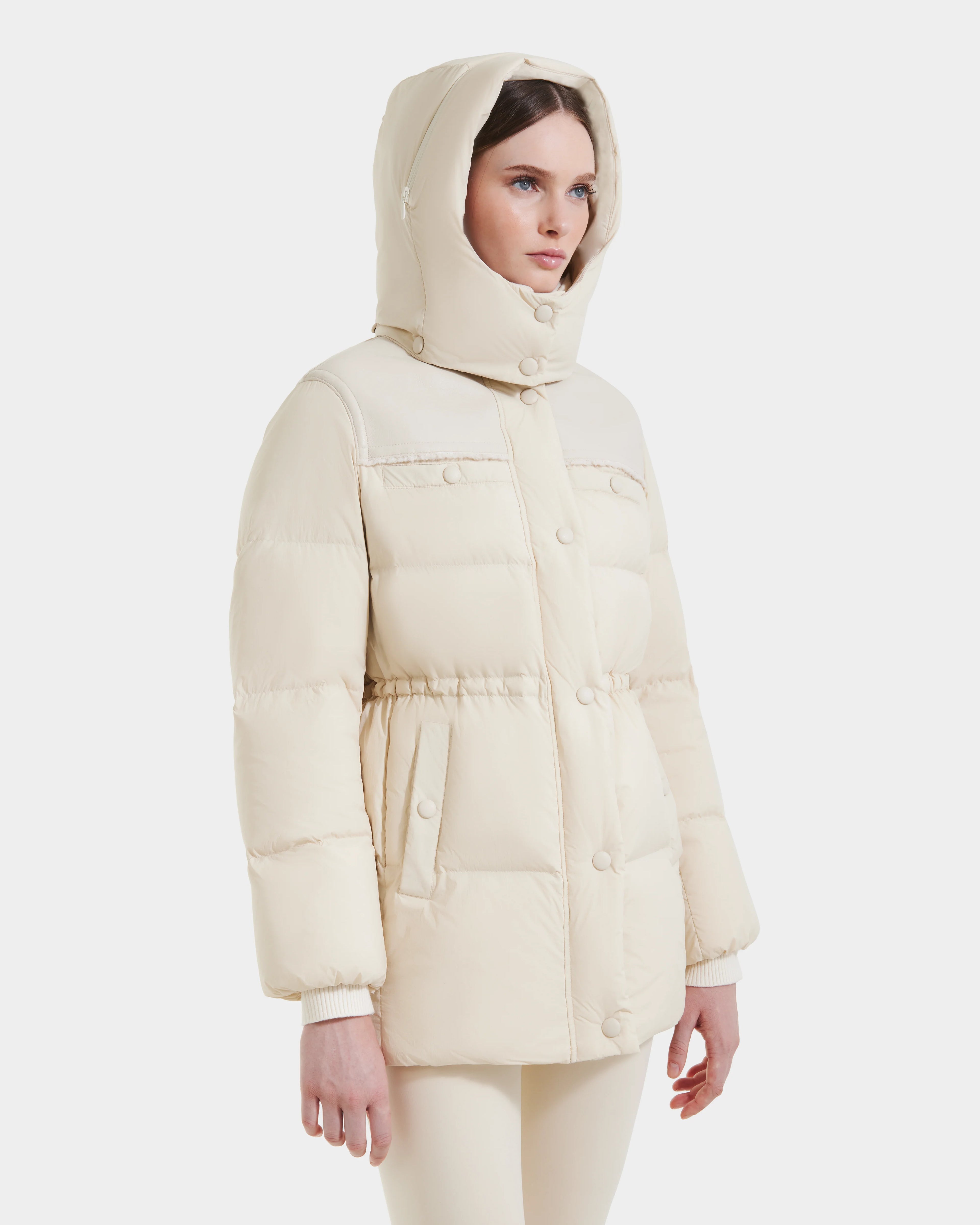 A woman stands against a plain white background wearing the Rudsak EMBER M-M - L125524 Vanilla down puffer jacket with front buttons and pockets.
