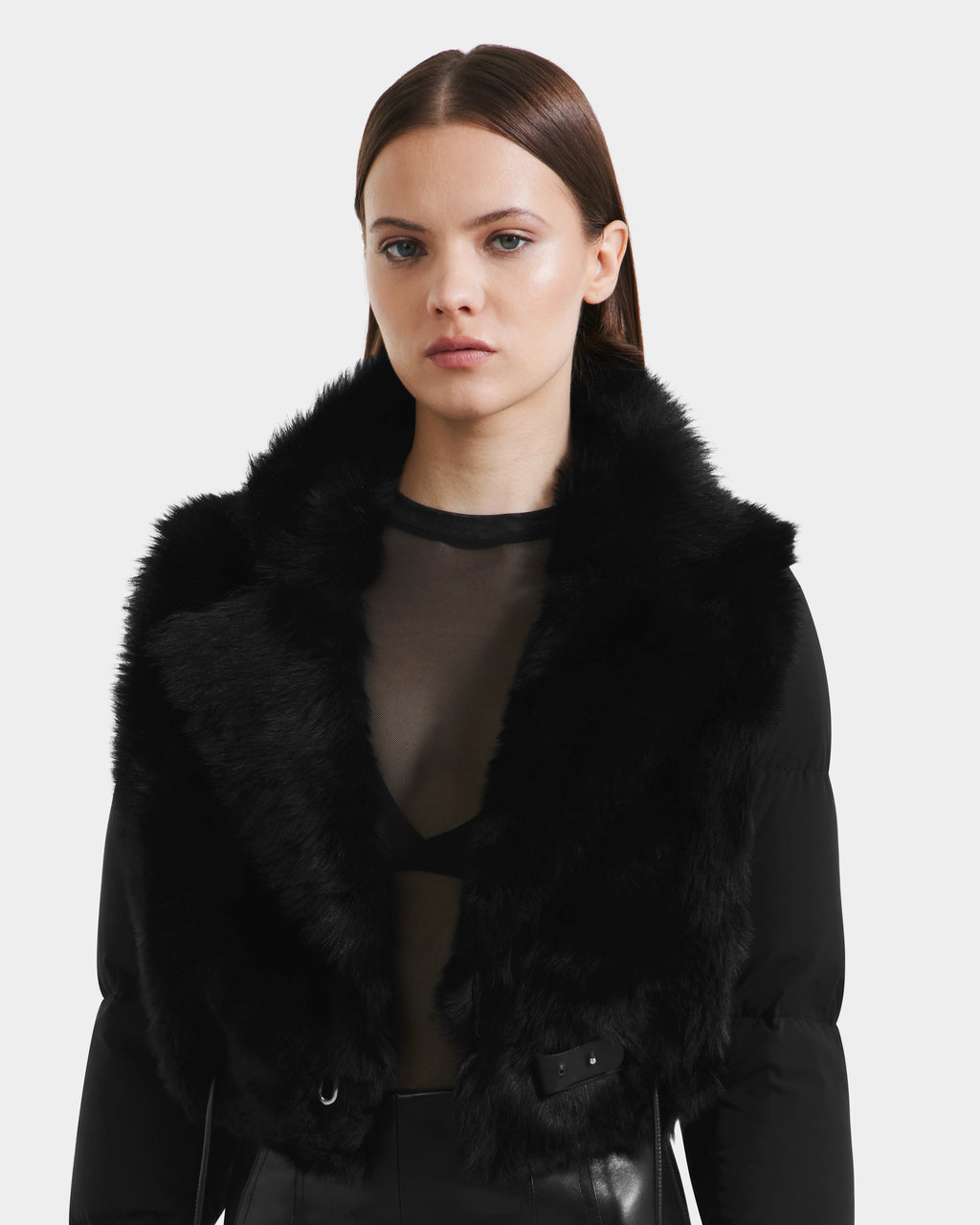A woman with straight brown hair models the Rudsak LILAH - 8125509 Black women’s cropped jacket with puffer sleeves, styled with a faux fur collar and sheer black top, against a plain white background.