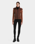 A woman faces forward against a white background, wearing the Rudsak MABS - 8125055 Rust puffer jacket with a hood, paired with a black turtleneck, black leggings, and black lace-up boots.