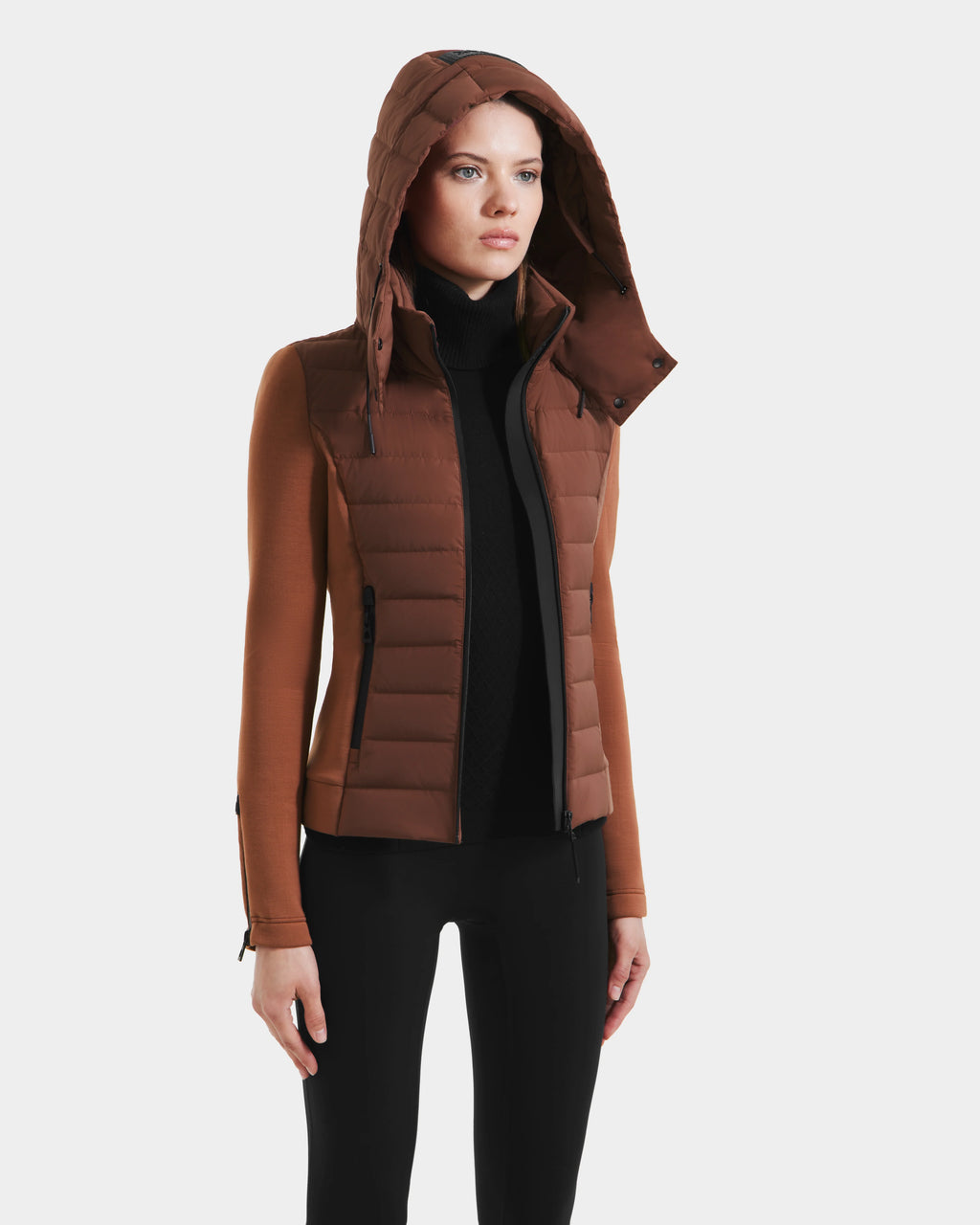 A woman wears the Rudsak MABS - 8125055 Rust RDS-certified down puffer jacket with zippered pockets, a black turtleneck, and black pants, standing against a plain white background.