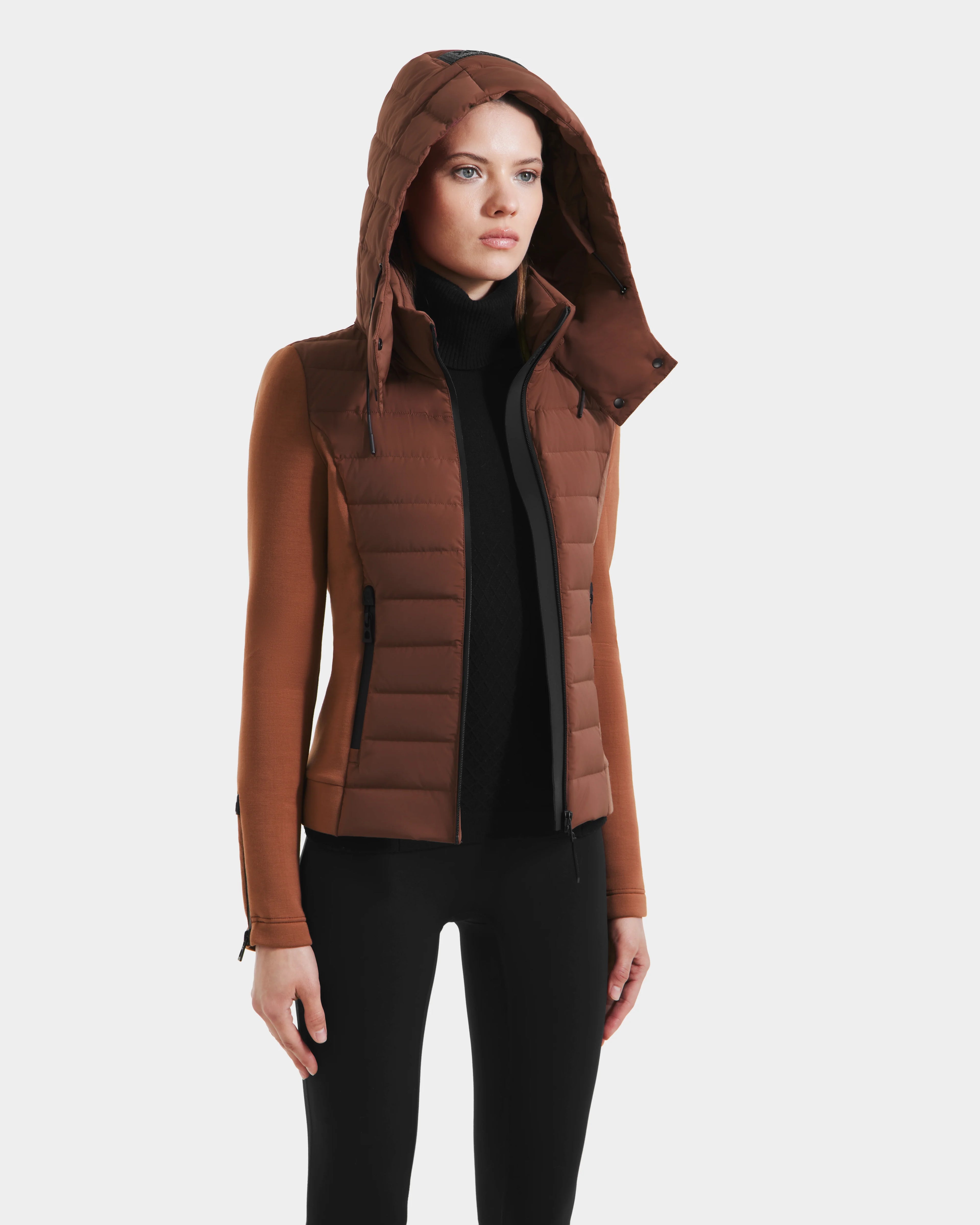 A woman wears the Rudsak MABS - 8125055 Rust RDS-certified down puffer jacket with zippered pockets, a black turtleneck, and black pants, standing against a plain white background.