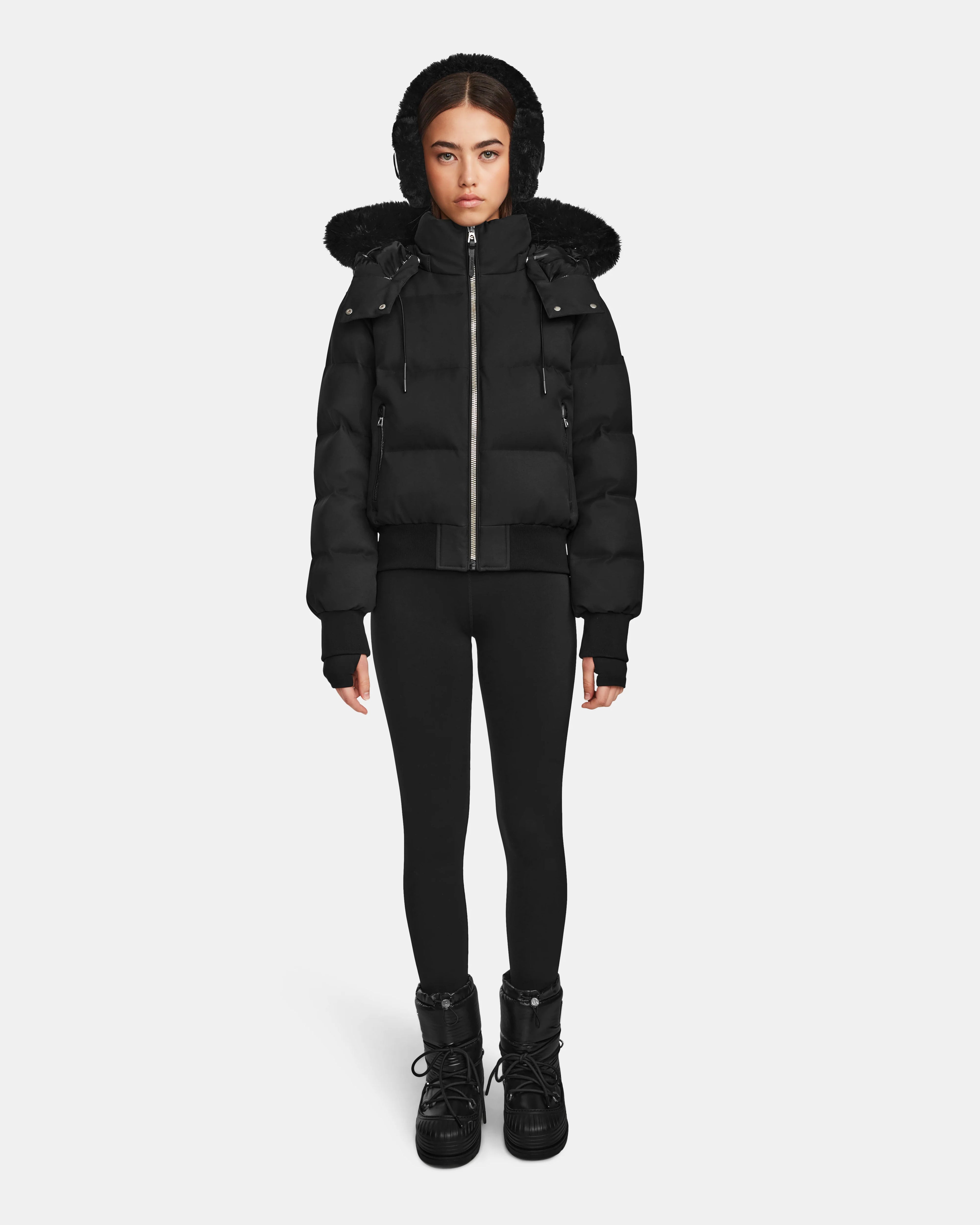 A woman faces forward against a plain white background wearing the Rudsak MAUDE Q-M - L124516 Black women's quilted down bomber, paired with black leggings and black winter boots.