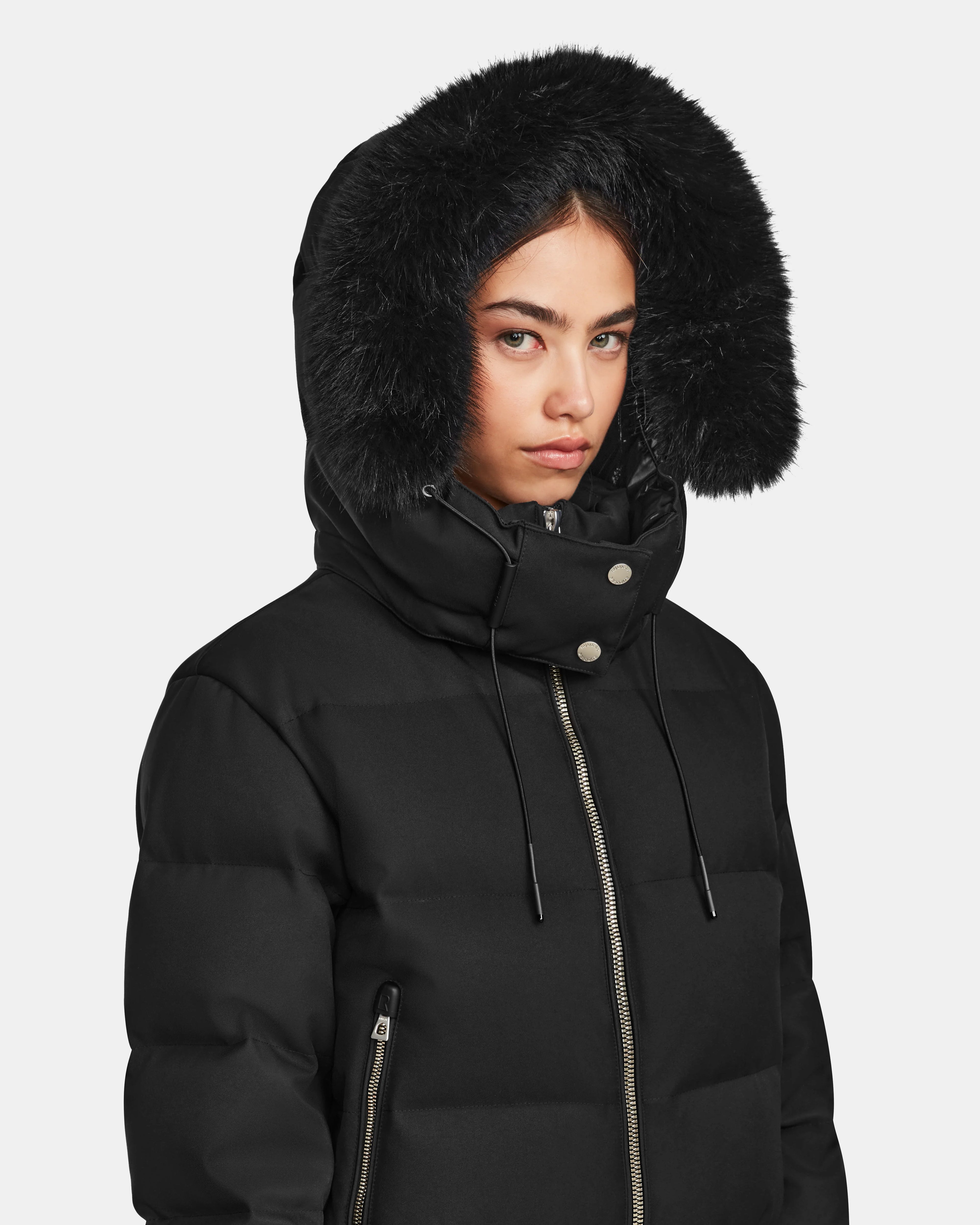 A woman in the Rudsak MAUDE Q-M - L124516 Black quilted down bomber with a fur-lined hood and RDS-certified down faces the camera. The winter jacket features a zipper, snap buttons, and is shown against a plain white background.
