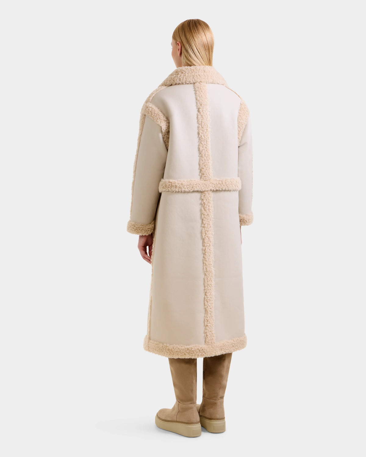 A person with straight, blonde hair is shown from the back wearing Rudsak’s PALOMA - 8125675 Vanilla reversible women’s coat in cream faux shearling with tan trim and matching boots, set against a plain white background.