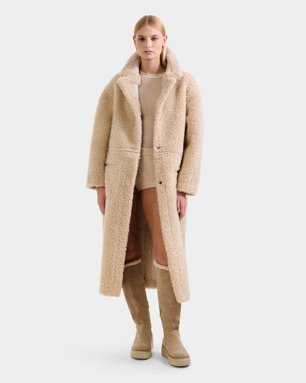 A woman faces forward wearing the Rudsak PALOMA - 8125675 Vanilla long beige textured faux shearling teddy coat over a nude top and shorts, styled with matching knee-high suede boots against a plain white background.