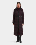 A woman with straight dark hair and a neutral expression wears the Rudsak PELIN L - 8124815 Bordeaux Mocha womens long down puffer, styled with a black belt, knee-high boots, and a high-neck burgundy top.