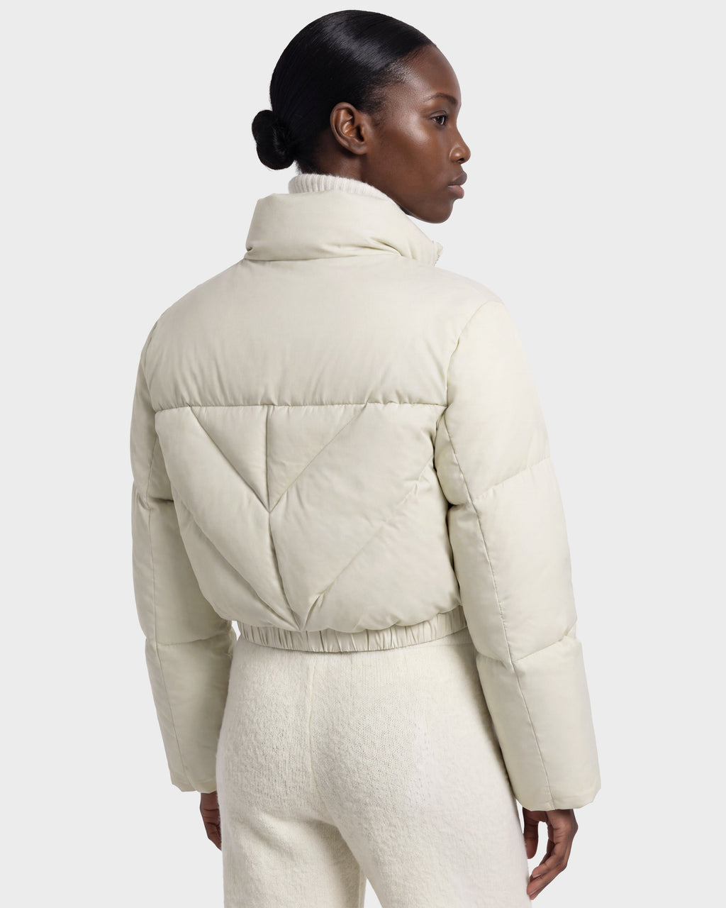 A person with dark hair in a low bun wears the Rudsak ANSLIE - 8126986 Vanilla, an RDS-certified down puffer jacket with matching pants, standing against a plain background and facing away from the camera.