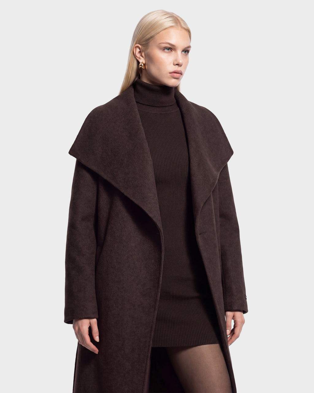 A woman with long blonde hair wears the CINDY - 8126526 Heather Cacao wool coat by Rudsak, featuring a wide collar, layered over a matching ribbed turtleneck dress, as she stands against a plain light background.