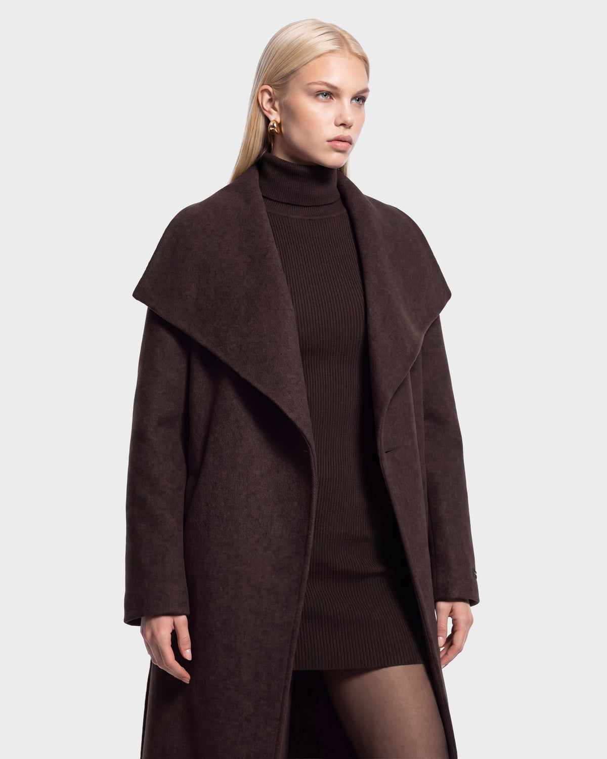 A woman with long blonde hair wears the CINDY - 8126526 Heather Cacao wool coat by Rudsak, featuring a wide collar, layered over a matching ribbed turtleneck dress, as she stands against a plain light background.
