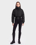 A person stands facing forward, wearing the Rudsak DONYA - 8126516 Black puffer jacket, styled with black leggings and tall black lace-up boots against a plain light gray background. This look is available for pre-order and is expected to ship by September 15th.