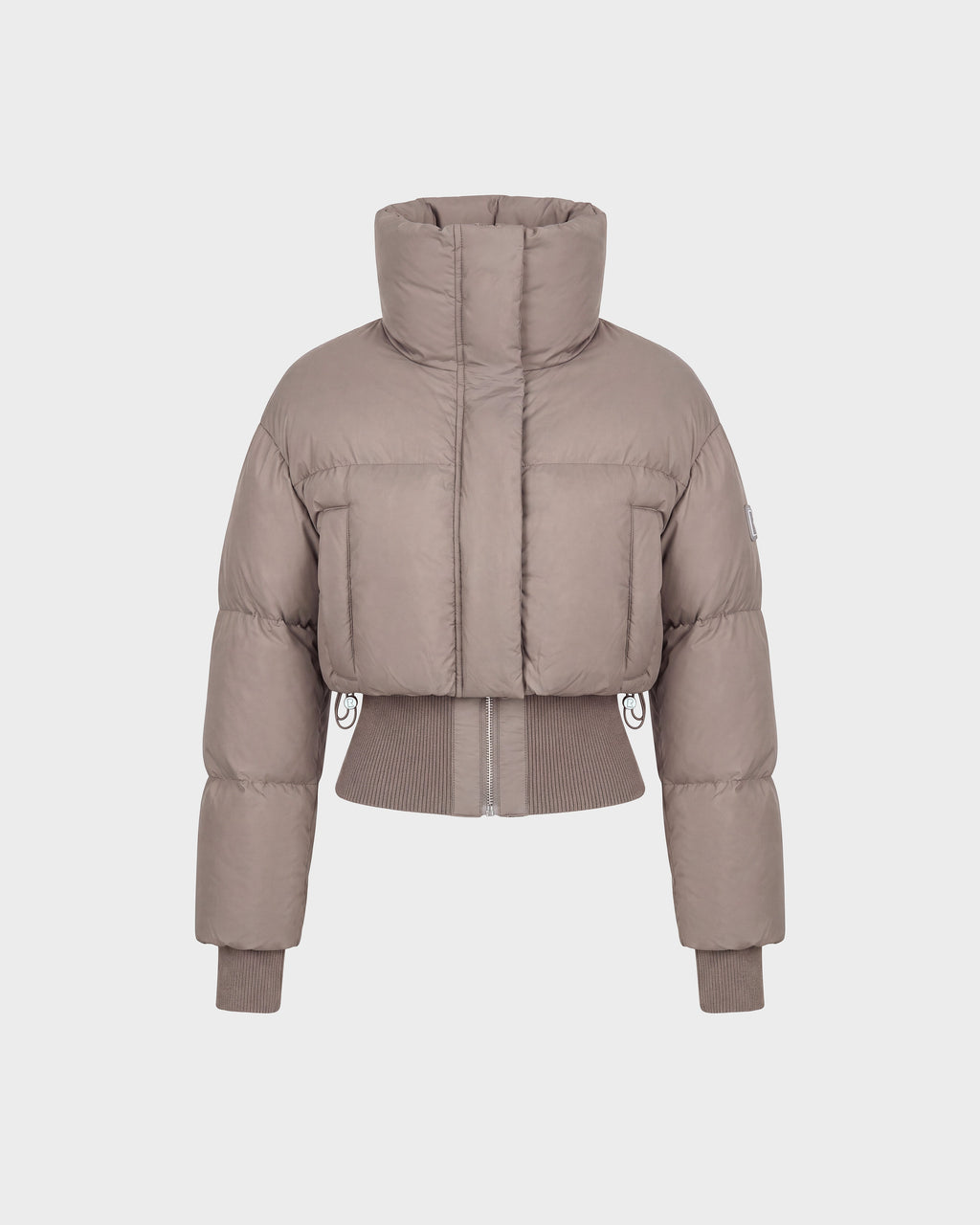 The Rudsak DONYA - 8126516 Cement is a taupe-colored, cropped women’s down puffer jacket made with RDS-certified down, featuring a high collar along with ribbed cuffs and hem, shown against a plain white background.
