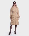 A woman stands against a plain white background wearing the ELVIE - 8126512 Almond quilted down trench coat by Rudsak—belted, tan-hued, and hooded, crafted for superior cold-weather performance with RDS-certified down—paired with oversized sunglasses, sheer black tights, and brown high heels.