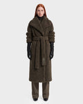 A woman with long red hair models the Rudsak FRANCIE - 8126873 Olive, a long, textured dark brown belted coat, layered over dark pants with black gloves and shoes. Photographed against a plain white background, this piece is available now for pre-order and expected to ship by September 15th.