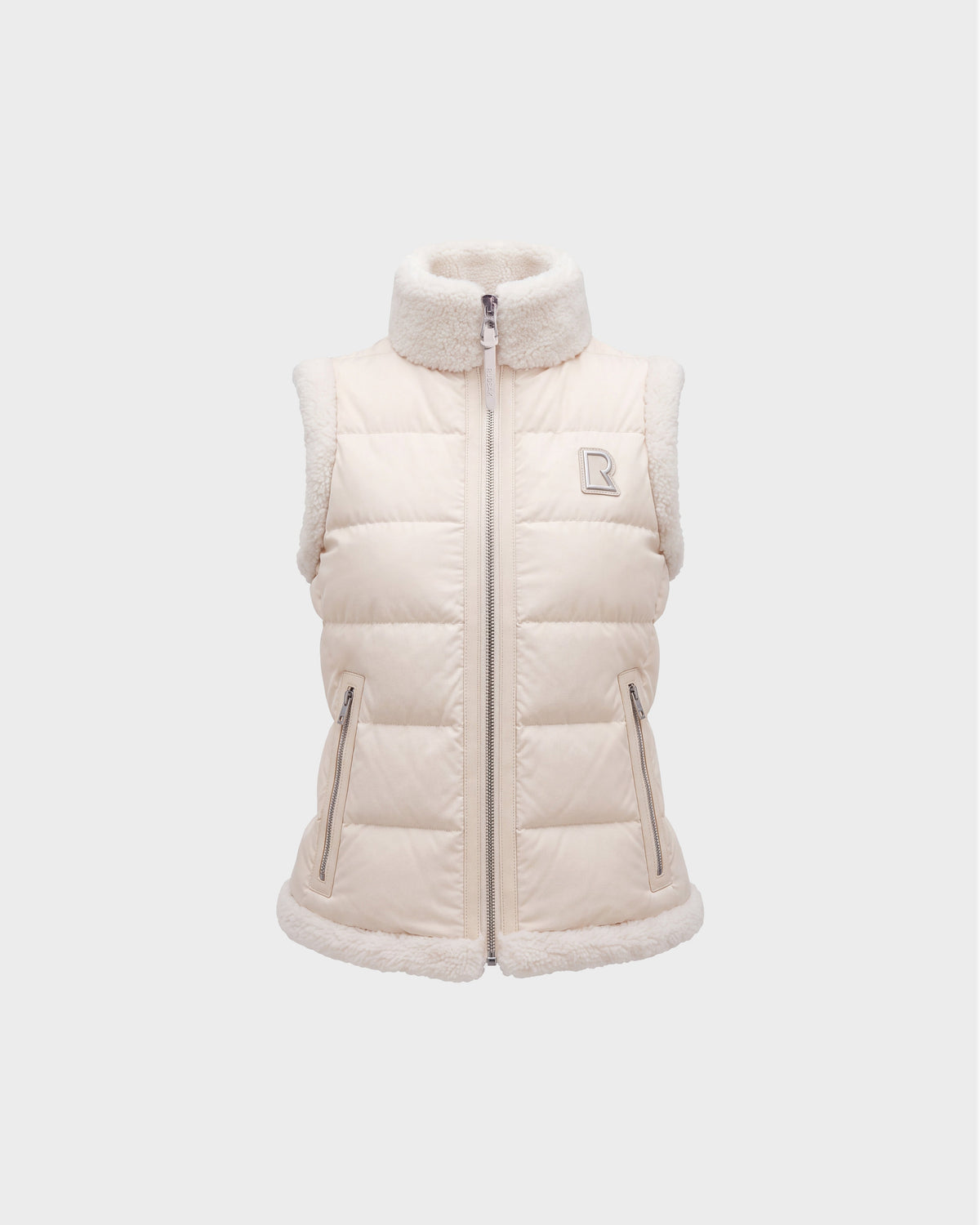 Introducing the HALI - 8126771 Vanilla by Rudsak: a cream-colored, sleeveless puffer vest featuring down insulation and sherpa lining on the collar, armholes, and hem. This vest includes a full zipper, two front zip pockets, and is finished with Rudsak’s signature small embroidered “R” logo on the left chest.