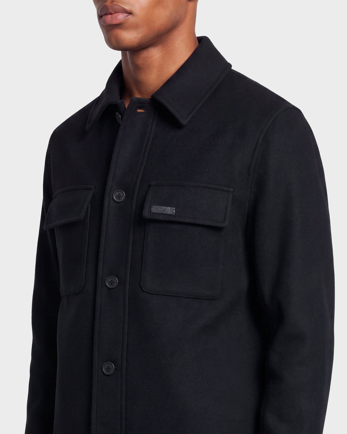 A person wearing the Rudsak MACKENZIE - 6126715 Black men’s wool-blend shirt jacket, featuring two front chest pockets, shown from shoulders to waist against a plain light background—perfect for transitional layering.