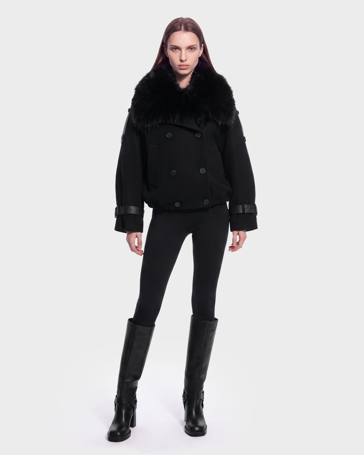 A person stands facing forward, wearing the MAEMI - 8126985 Black jacket by Rudsak, paired with black leggings and knee-high black boots, against a plain white background. This stylish look is available for pre-order and is expected to ship by September 15th.