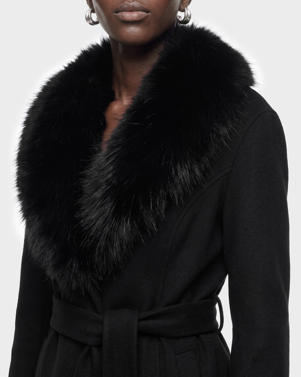 A person wearing the Rudsak MARILLA WL - 8126737 Black coat, featuring a large, fluffy black fur collar and a waist tie, is shown from the shoulders to mid-torso against a plain background. This item is available for pre-order and is expected to ship by September 15th.