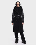 A woman is wearing the Rudsak NOELLE - 8126971 Black double-breasted coat, featuring textured fabric and subtle faux fur accents. She pairs it with black pants, black boots, and earmuffs, standing against a plain white background with a neutral expression.