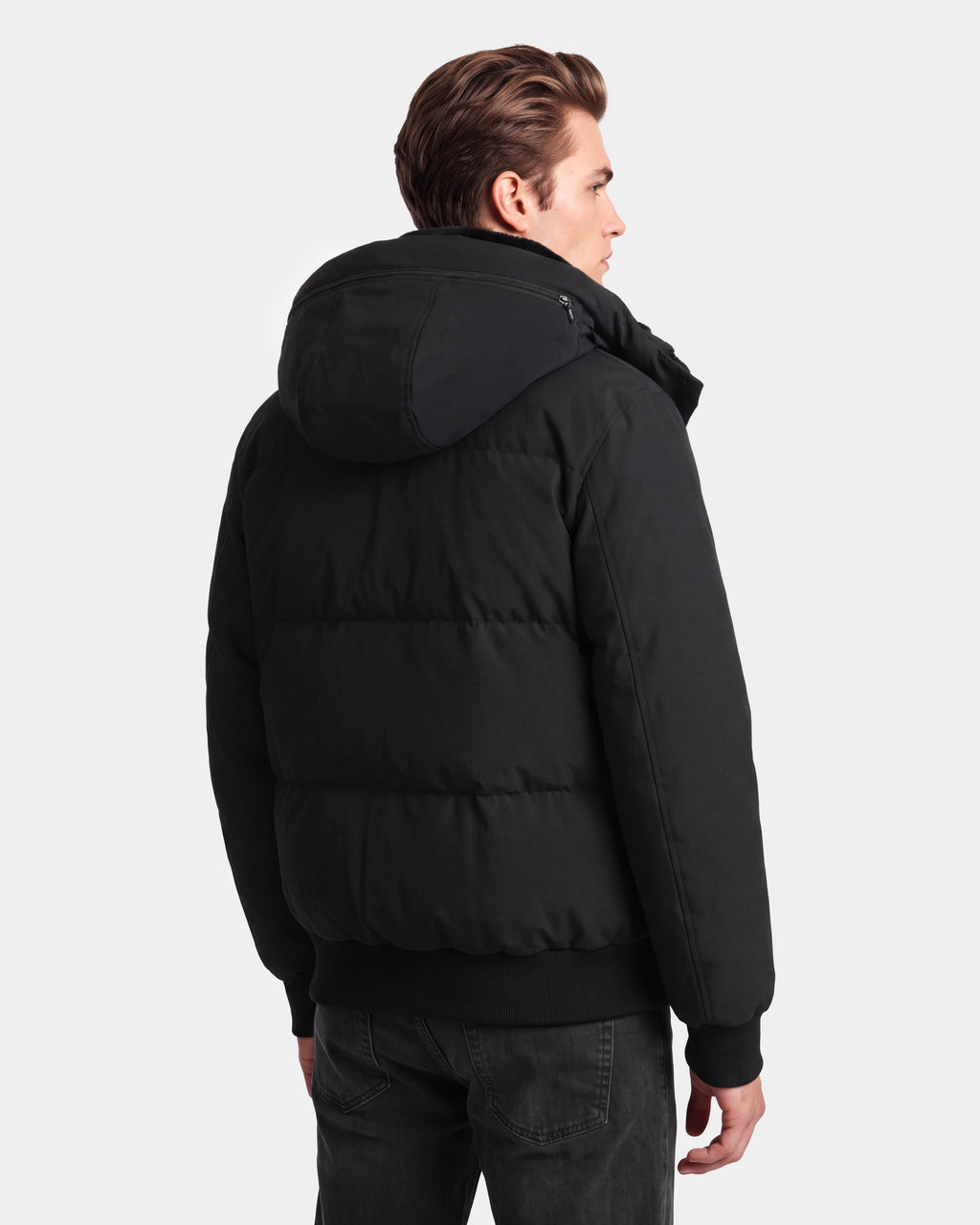 A person with light brown hair, wearing the Rudsak WILL - 6126561 Black puffer jacket with a hood and dark jeans, stands facing away against a plain white background.