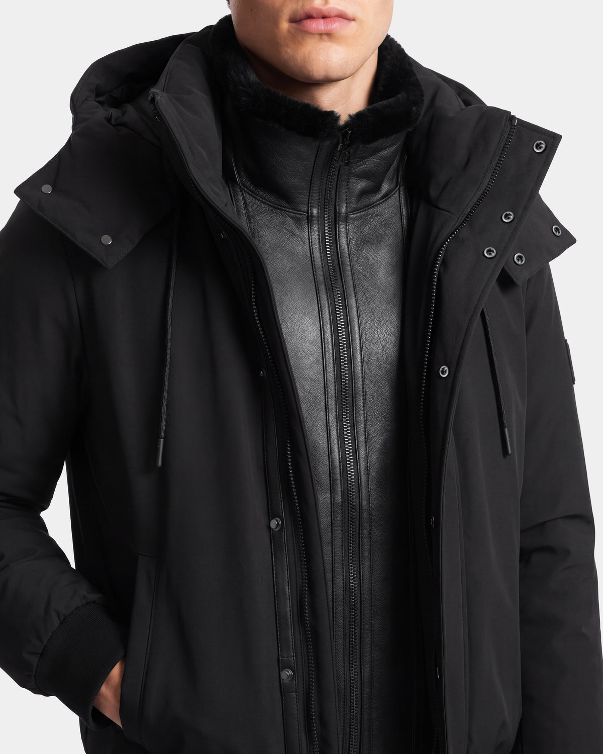 A person wearing the Rudsak WILL - 6126561 Black hooded jacket layered over a black leather zip-up jacket, shown from the shoulders to the mouth against a plain background.