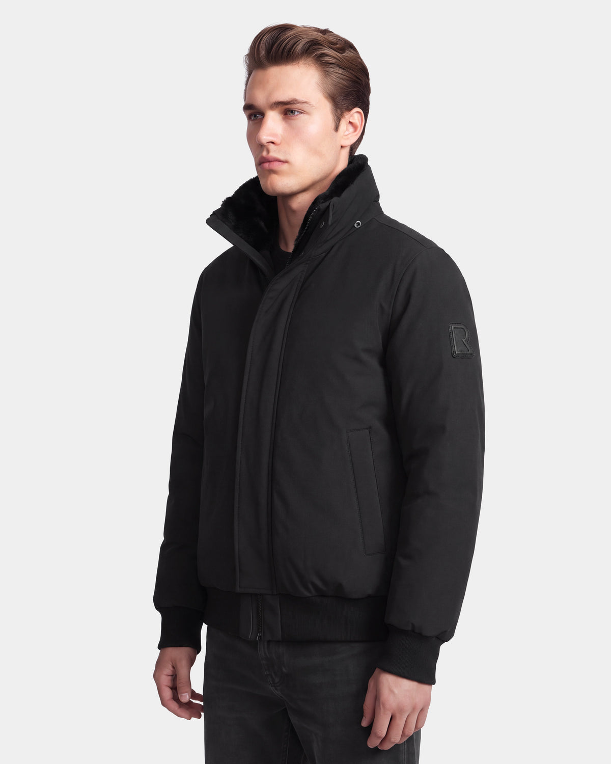 A man wearing the Rudsak WILL - 6126561 Black zip-up winter jacket with a high collar and black pants stands facing slightly to the side against a plain light background.