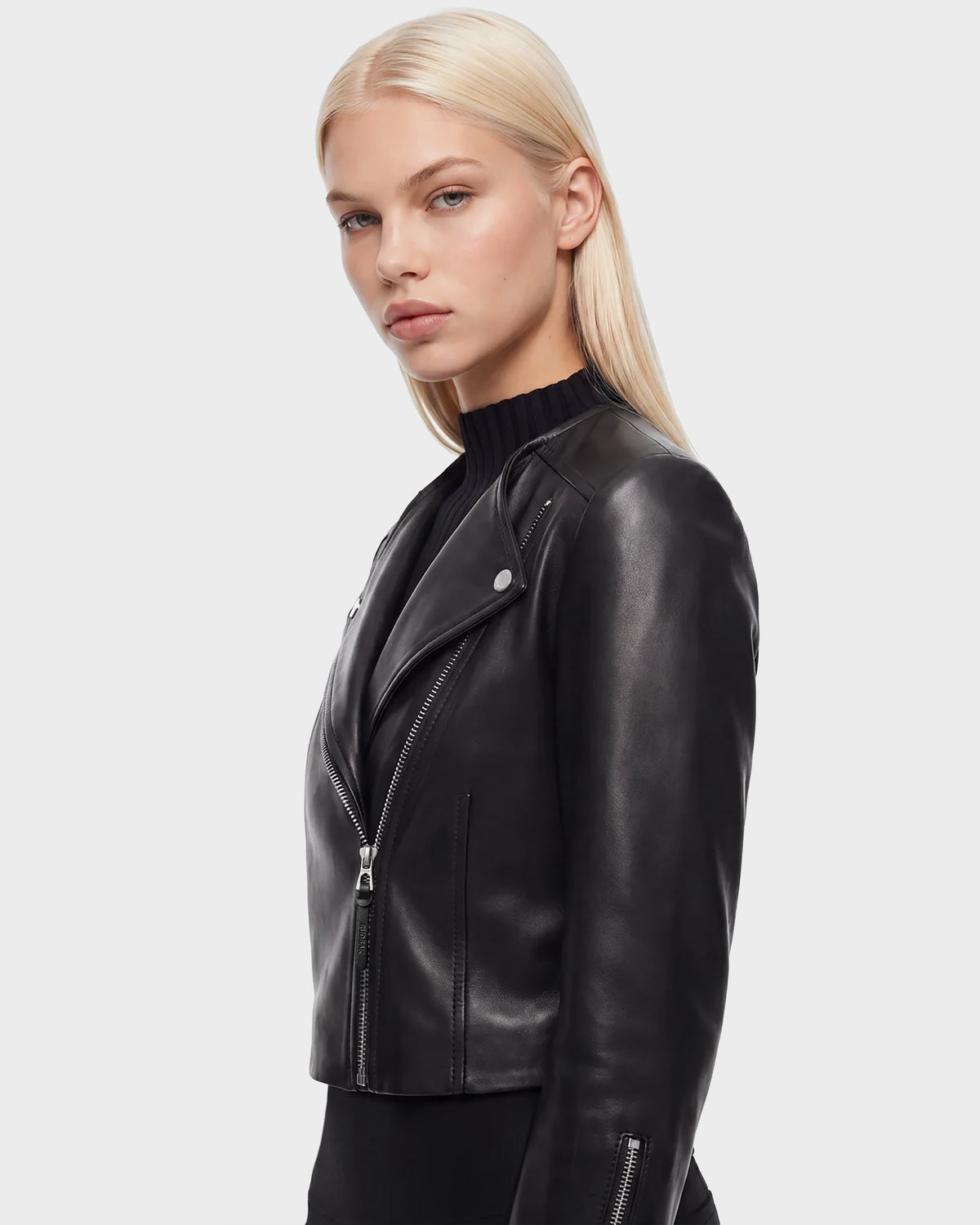 A woman with straight blonde hair wears the WINNI - 8124053 Black women's leather jacket by Rudsak over a black top, standing against a plain light gray background and looking slightly to the side with a neutral expression.