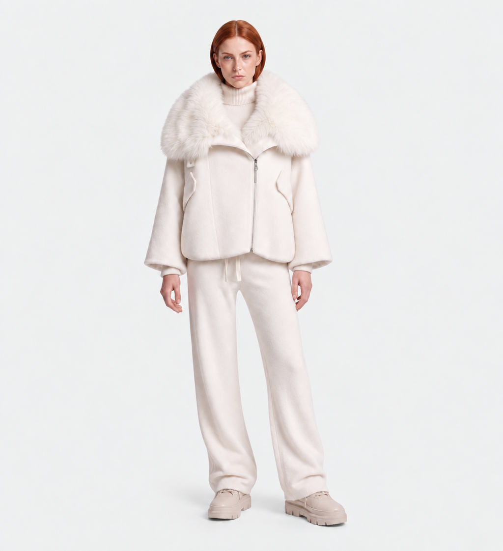 A person stands facing forward in the ZARIA - 8126999 Vanilla by Rudsak, a white puffer with a faux-fur collar, paired with a white turtleneck, matching pants, and beige shoes against a plain light background.