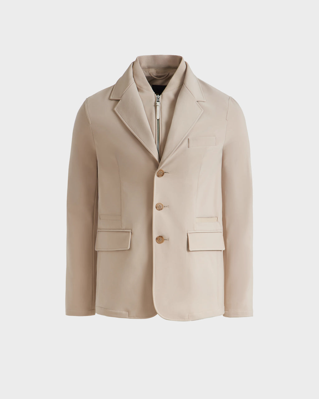 The Rudsak KEITH - 6125045 Almond is a beige blazer-style jacket with notch lapels, three brown buttons, two front flap pockets, a chest pocket, and an inner zip-up layer—modern tailoring shown on a white background.