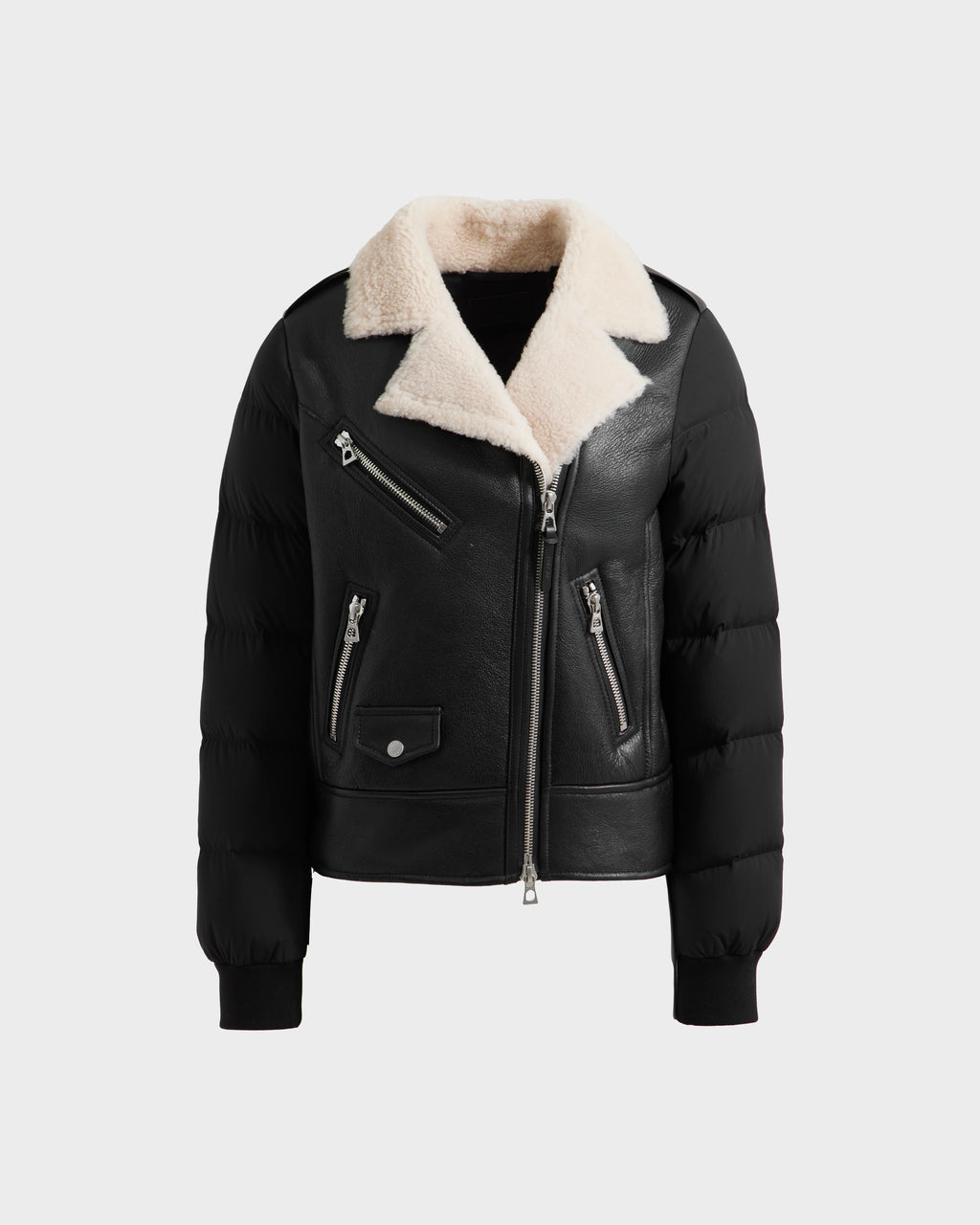 The Rudsak MALA - 8125628 Black is a women’s cropped black leather shearling jacket with puffer sleeves, silver zippers, two side pockets, a chest pocket, and an off-white shearling collar, shown on a plain light gray background.