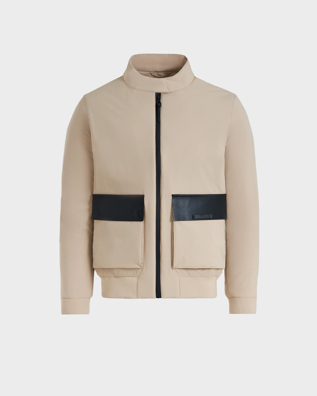 The Rudsak PETER - 6125001 Almond is a lightweight beige bomber jacket with a high collar, front zipper, and two large beige pockets with black flaps, featuring modern design details and vegan leather accents against a white background.