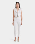 A woman stands facing forward in the Rudsak BETTY - 8125000 Optic White sleeveless leather vest, high-waisted white pants with ankle front slits, and white pointed-toe shoes against a plain white background.