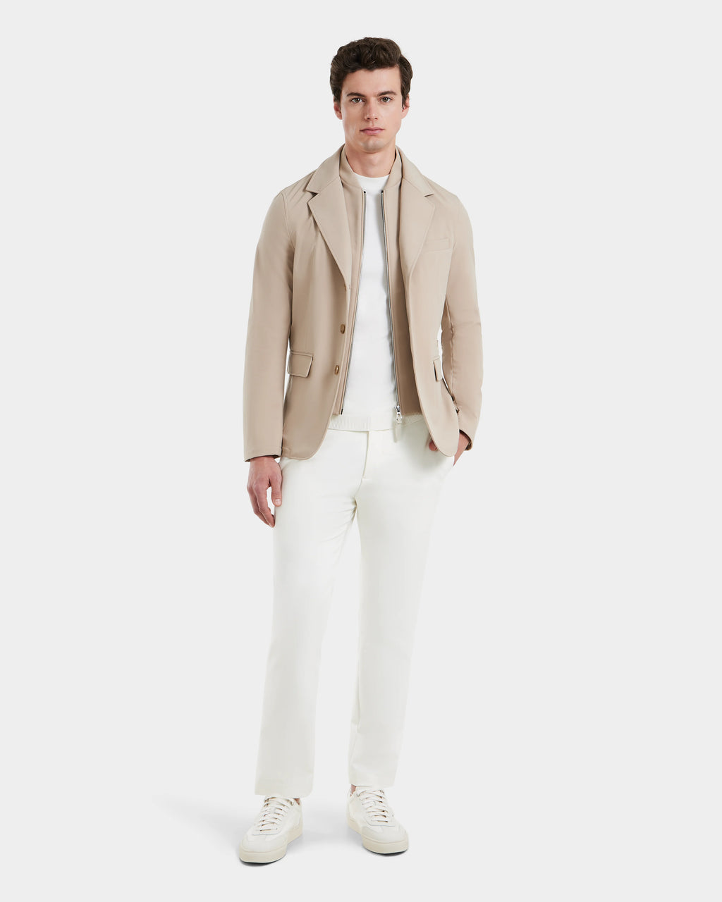 A man faces forward against a white background, showcasing Rudsaks KEITH - 6125045 Almond blazer-style jacket over a white shirt, off-white pants, and white sneakers.