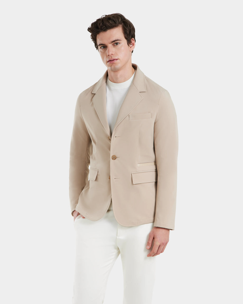 A man models the Rudsak KEITH - 6125045 Almond blazer-style jacket over a white shirt and pants, standing against a plain light background and gazing at the camera with a neutral expression.