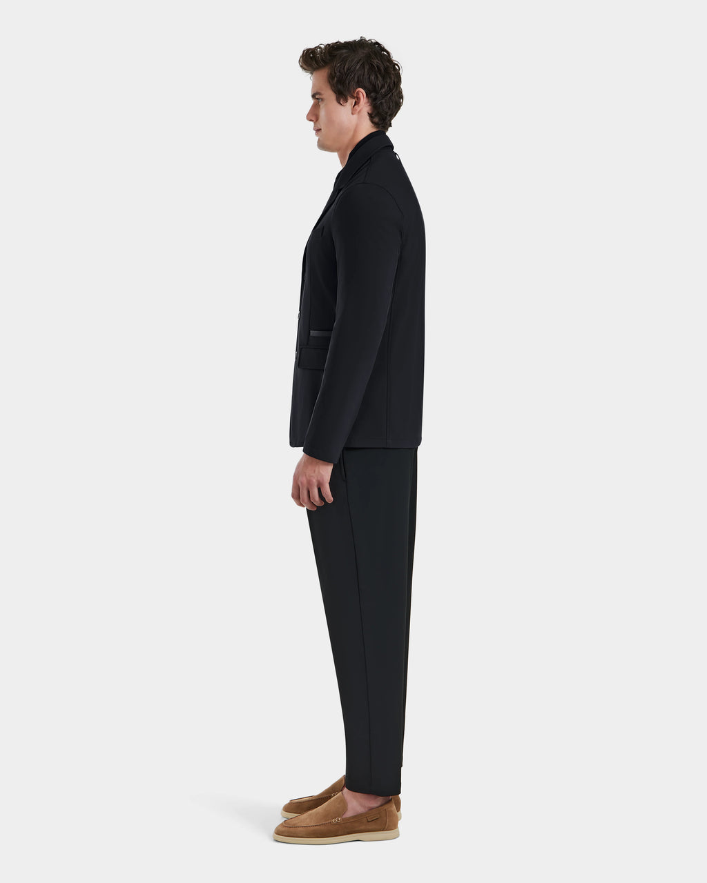 A man stands in profile facing left, wearing the Rudsak KEITH - 6125045 Black blazer-style jacket with a black suit and tan loafers, set against a plain white background.