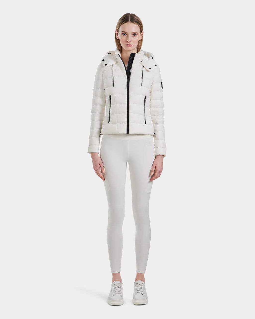 A woman stands facing forward, wearing the Rudsak MELISSA - 8124031 Cotton White lightweight down puffer jacket and matching fitted pants with white sneakers against a plain white background.